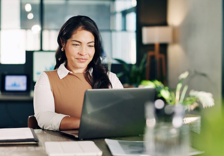A business professional reviewing financial records and documentation on a laptop in an office setting.