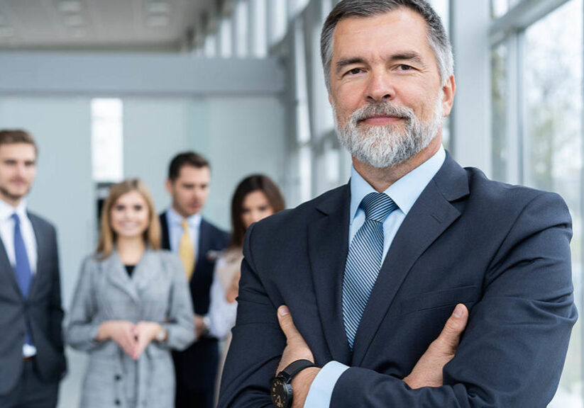 Senior businessman in office standing in front of the team