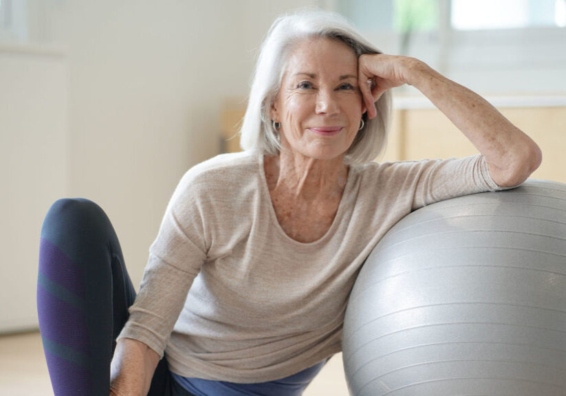 Smiling senior woman resting on a swiss ball at home