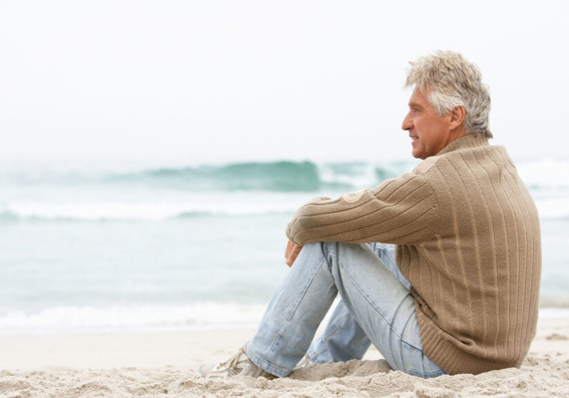 Man sitting on a beach viewing the calm waters
