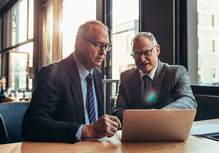 Two financial professionals in suits reviewing information on a laptop in a modern office, discussing private credit investment strategies.