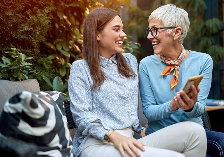 Mother and adult daughter smiling while discussing family legacy and estate planning on a smartphone outdoors