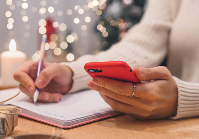 Woman's hands with pen and mobile phone writing out a checklist