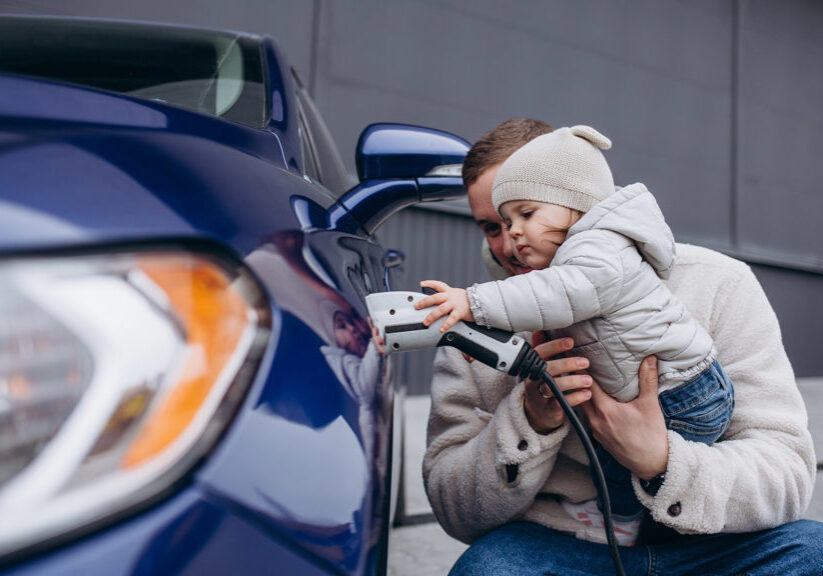 father playing with young daughter while charging electric car