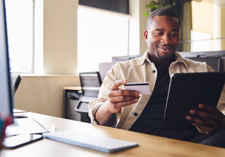 A person holding a credit card while looking at a tablet, representing credit card fraud prevention.