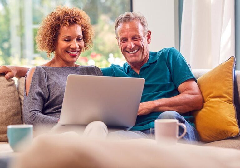 Mature couple smiling while reviewing investment and tax planning strategies on a laptop, representing an enhanced direct indexing approach for high-net-worth portfolios.
