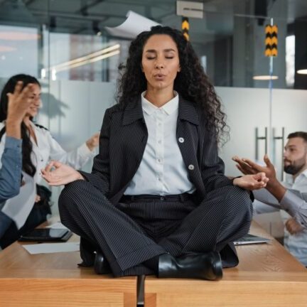 Business woman keeping calm while sitting on top of a table during chaotic meeting.