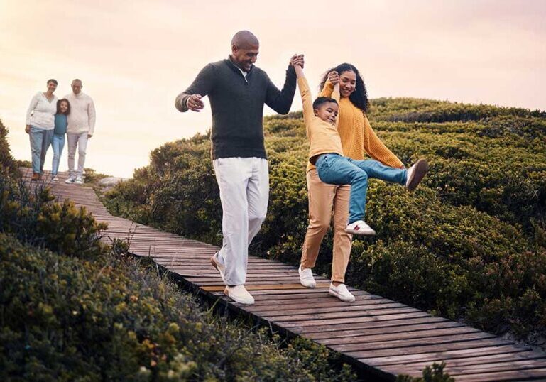 Multigenerational family walking and laughing along a wooden boardwalk in nature, representing legacy and estate tax planning