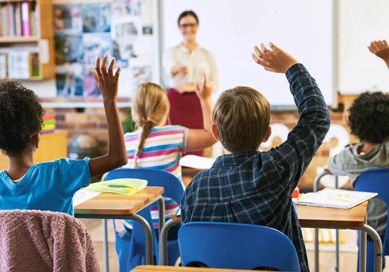 Education, question with group of children in classroom and raise their hands to answer. Learning or support, diversity and teacher teaching with young students in class of school building together.