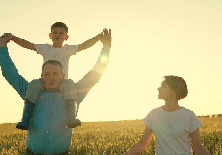 a little boy sits riding on his father's shoulders in a wheat field. dad farmer farming. happy family walks at sunset in the field. childhood dream happy family. child plays pilot flight sky. dream boy teamwork family.