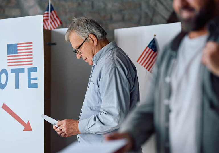 Senior man with a ballot at voting booth during US election