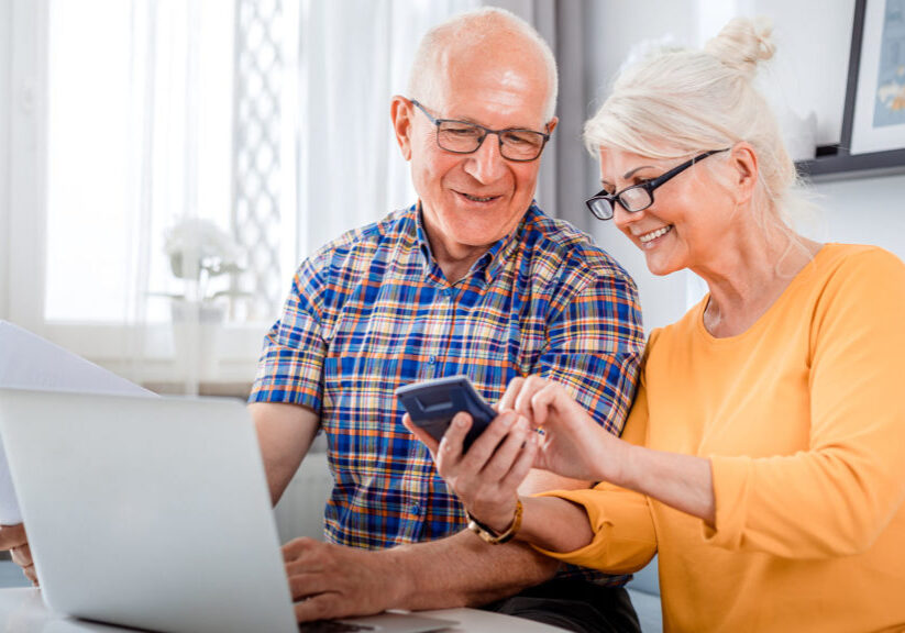 Senior couple looks at information on their laptop and cell phone