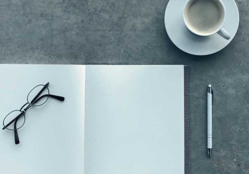 Reading glasses on top of notepad with pen and coffee cup