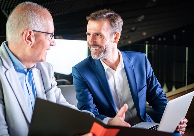 An older business owner reviews a folder with a Creative Planning business exit planning advisor who holds a laptop in a modern office.
