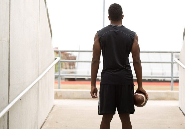 College football player holding a football and walking out of the tunnel toward the stadium field