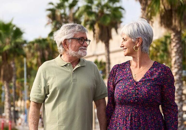 Retired couple smiling and walking outdoors along a palm tree-lined sidewalk, illustrating considerations for retirement relocation.